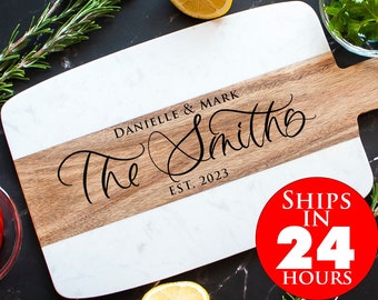May include: White and brown rectangular cutting board with a marble design. The board has a wooden handle and is personalized with the text "The Smiths Est. 2023".