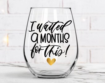 May include: A clear glass wine glass with a black vinyl decal that reads "I waited 9 months for this!" with a gold heart below the text.