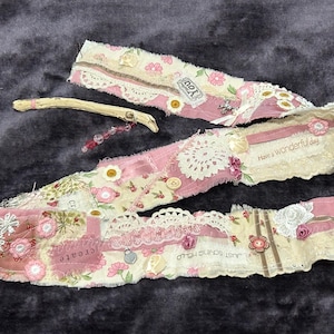May include: A pink and white fabric banner with lace trim and floral patterns. The banner has the text "Have a wonderful day" and "Just Breathe" on it.