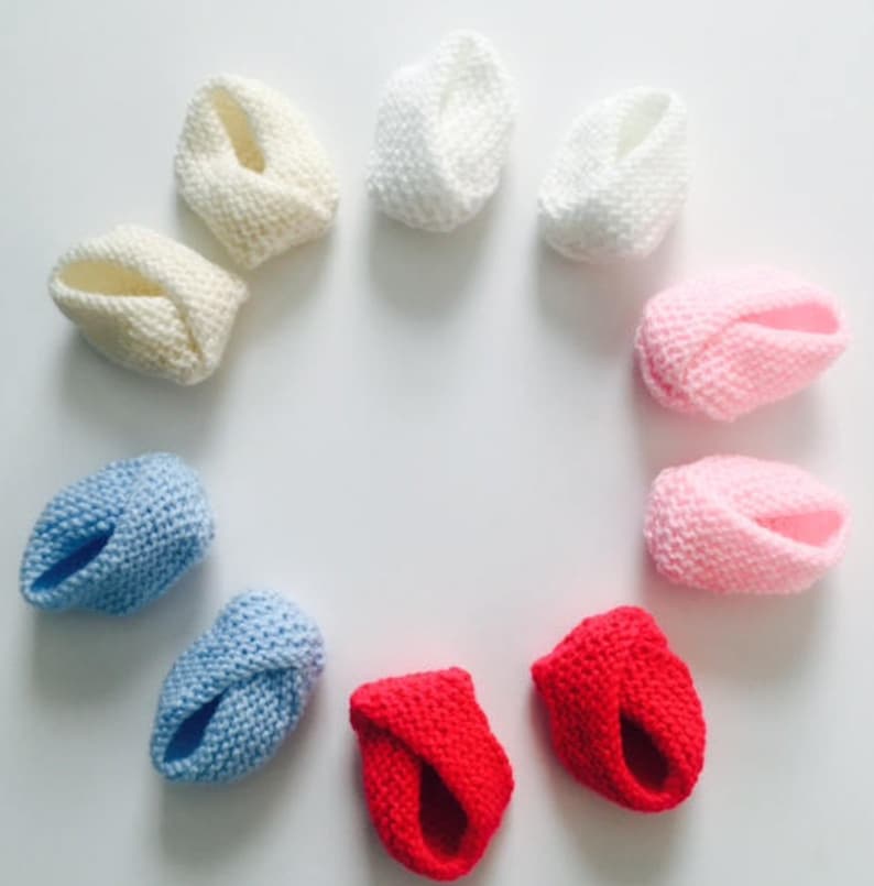 Puede incluir: Una colecci&oacute;n de patucos de beb&eacute; hechos a mano en una variedad de colores, incluyendo blanco, crema, rosa, azul y rojo. Los patucos est&aacute;n dispuestos en un patr&oacute;n circular, mostrando su textura y dise&ntilde;o de punto. Estos patucos suaves y acogedores son perfectos para reci&eacute;n nacidos.