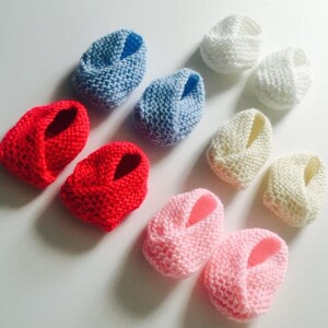 Puede incluir: Varios patucos de beb&eacute; tejidos a mano en rojo, azul claro, blanco, crema y rosa. El tejido suave y texturizado sugiere un dise&ntilde;o acogedor y c&oacute;modo para beb&eacute;s.