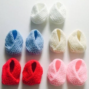 Puede incluir: Ocho pares de patucos de beb&eacute; de punto en varios colores. Los patucos est&aacute;n dispuestos en pares, mostrando tonos blancos, azules, crema, rojos y rosas. El tejido de punto suave y texturizado sugiere una sensaci&oacute;n acogedora y hecha a mano, ideal para reci&eacute;n nacidos.