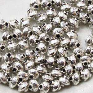 May include: A large quantity of silver metal beads with a decorative swirl pattern. The beads are round and have a hole in the center for stringing.