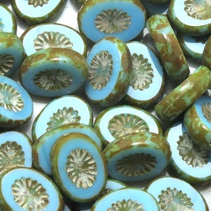 May include: A collection of oval-shaped glass beads with a light blue and green color scheme. The beads have a raised, silver-colored design in the center.