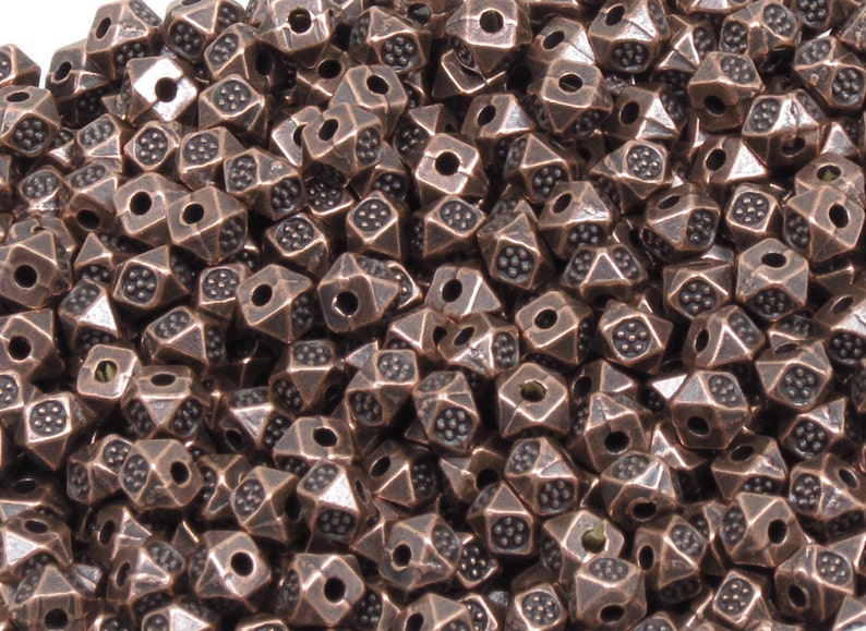 K&ouml;nnte beinhalten: Ein gro&szlig;er Haufen kupferfarbener Metallperlen. Jede Perle hat eine Pyramidenform mit einem Loch in der Mitte. Die Perlen haben eine strukturierte Oberfl&auml;che.