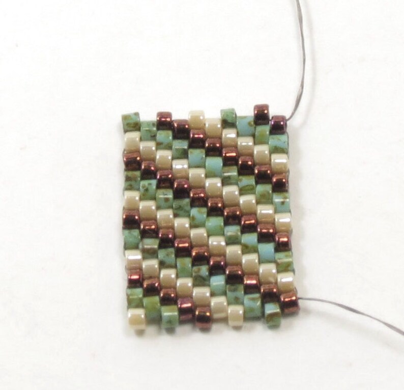 May include: A small square of beadwork with a geometric pattern. The beads are in shades of brown, green, and cream.