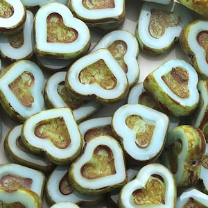 May include: A collection of heart-shaped glass beads with a light blue glaze and a brown, marbled pattern. The beads are perfect for jewelry making or crafting.