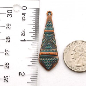 May include: A copper-colored pendant with a turquoise and copper geometric design. The pendant is about 1 inch long and is shown next to a US quarter for size comparison.