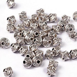 May include: A large group of silver metal beads with intricate designs. The beads are all the same size and shape, and they have a shiny finish.