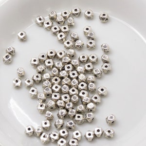 May include: A pile of silver metal beads with a flower design on each bead. The beads are scattered on a white surface.