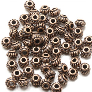 May include: A pile of antique copper-toned metal beads with a decorative swirl design. The beads have a hole in the center for stringing.