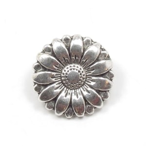 May include: A silver-toned metal daisy-shaped button. The button features detailed petals surrounding a textured center. The button is round and has a slightly aged appearance, suggesting a vintage or antique style.