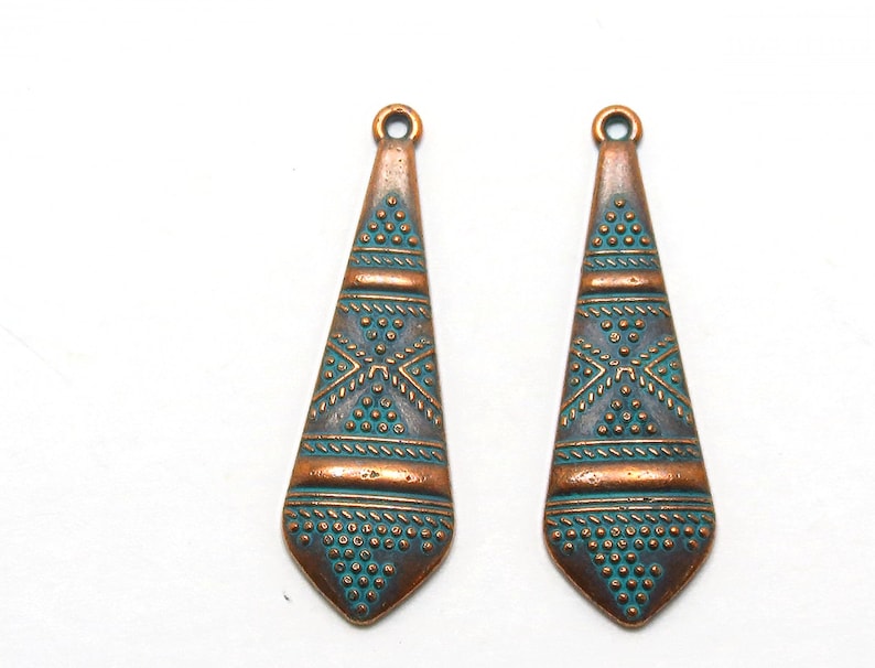May include: Two copper-colored pendant charms with a teal blue geometric design. The charms are shaped like a teardrop and have a small loop at the top for attaching to jewelry.