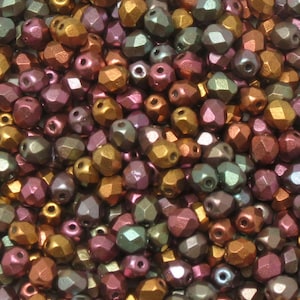May include: A close-up view of a collection of faceted beads in various colors. The beads have a metallic finish and are in shades of gold, bronze, purple, and green. The beads are small and have a hole for stringing.