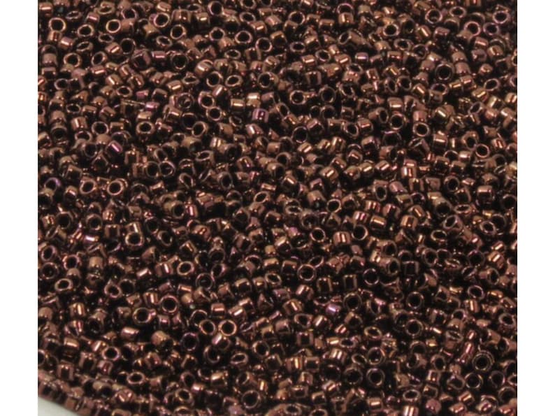 May include: A close-up view of a large quantity of small, round, dark brown seed beads. The beads have a metallic sheen and are scattered randomly.