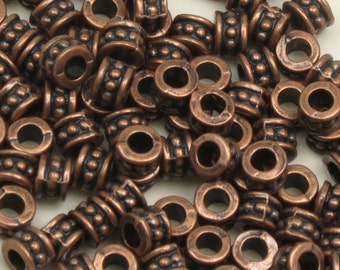 May include: A large pile of copper-colored metal beads with a textured design. The beads have a small hole in the center and are perfect for jewelry making.