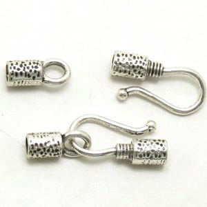 May include: Silver-toned jewelry clasps with a textured barrel design and a hook closure. The clasps are shown in various configurations, including a single barrel with a loop, and two clasps connected.