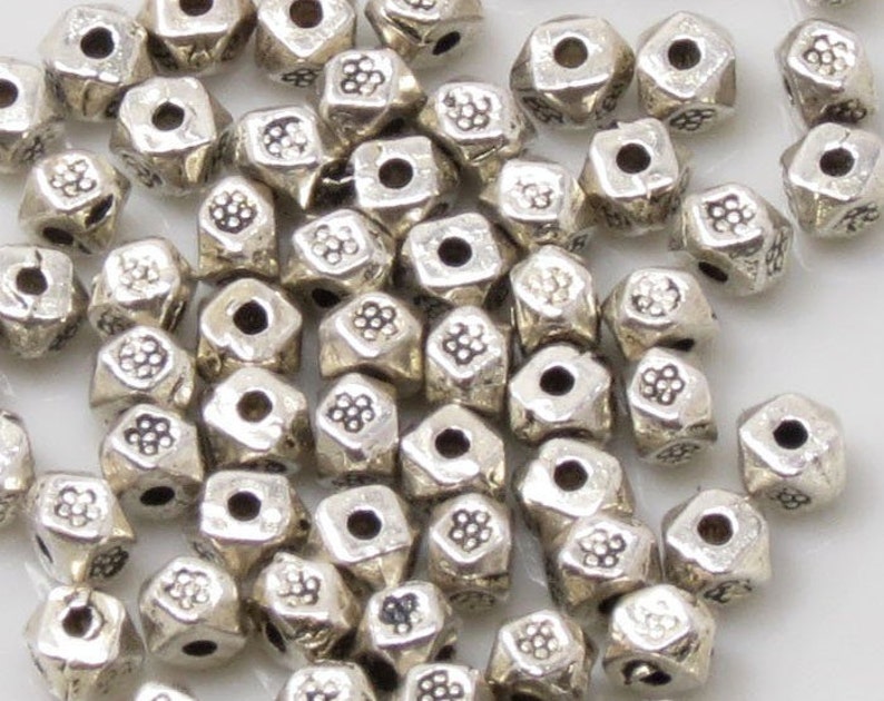 May include: A close-up of a pile of silver metal beads. The beads are hexagonal in shape and have a textured surface.