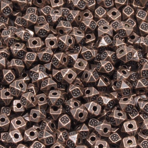 K&ouml;nnte beinhalten: Ein gro&szlig;er Haufen kupferfarbener Metallperlen. Jede Perle ist ein Quadrat mit einer spitzen Oberseite und einem Loch in der Mitte.