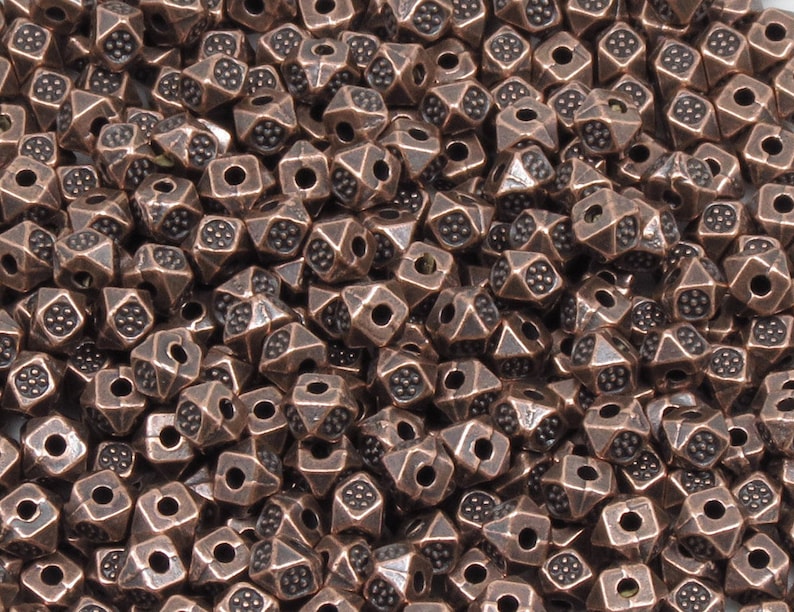 K&ouml;nnte beinhalten: Ein gro&szlig;er Haufen kupferfarbener Metallperlen. Jede Perle ist ein Quadrat mit einer spitzen Oberseite und einem Loch in der Mitte.
