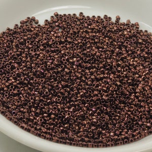 May include: A close-up view of a large quantity of small, round, copper-colored beads. The beads are arranged in a random pattern and fill the entire image.