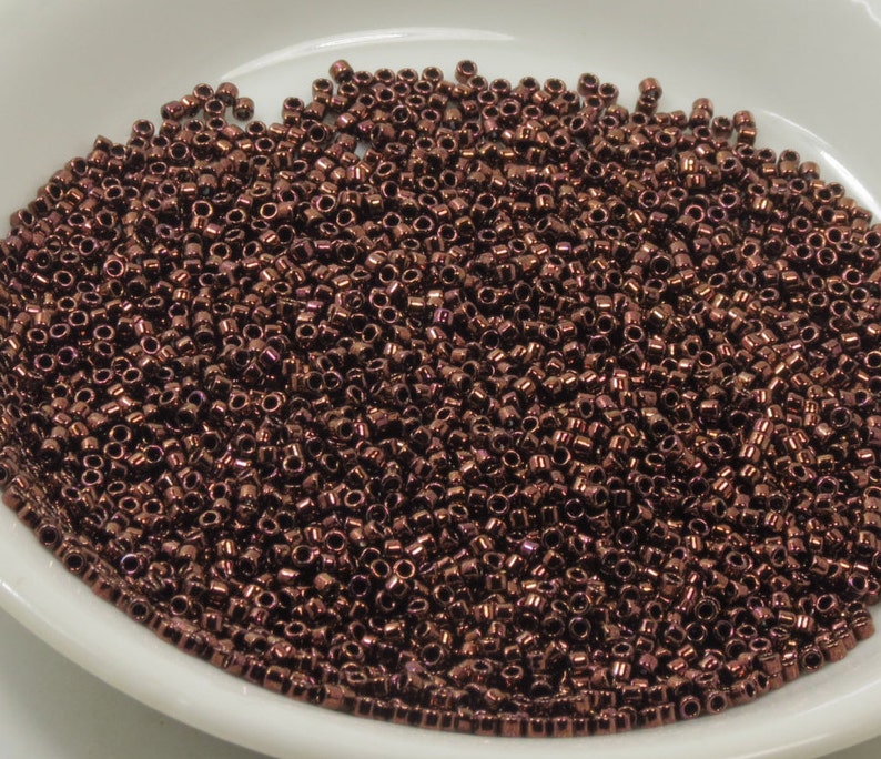 May include: A close-up view of a large quantity of small, round, copper-colored beads. The beads are arranged in a random pattern and fill the entire image.