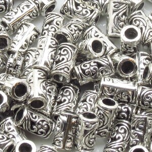 May include: A pile of silver metal bead caps with an ornate design. The caps have a hole in the center and are designed to be used as end caps for jewelry making.