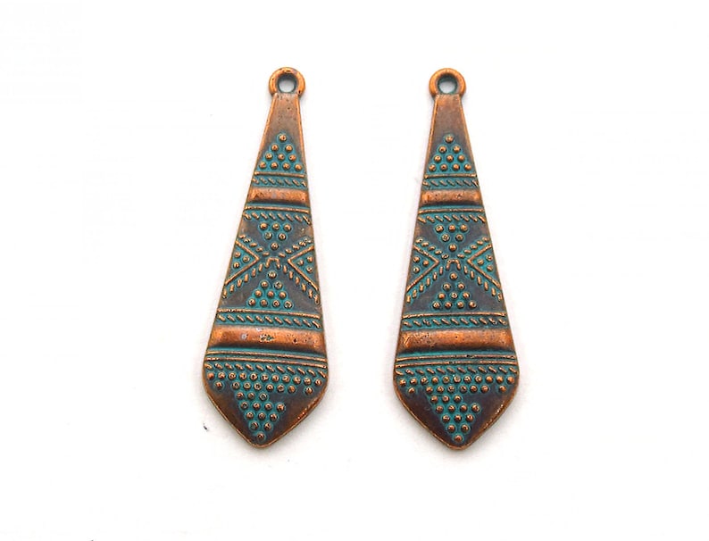 May include: Two copper-colored teardrop-shaped pendant charms with a turquoise-colored geometric design.