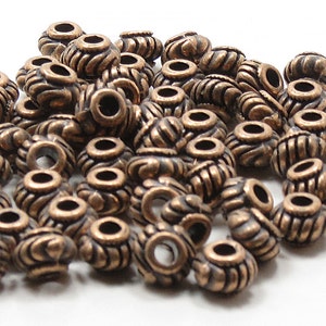 May include: A pile of antique copper-colored beads with a decorative design. The beads have a hole in the center for stringing.