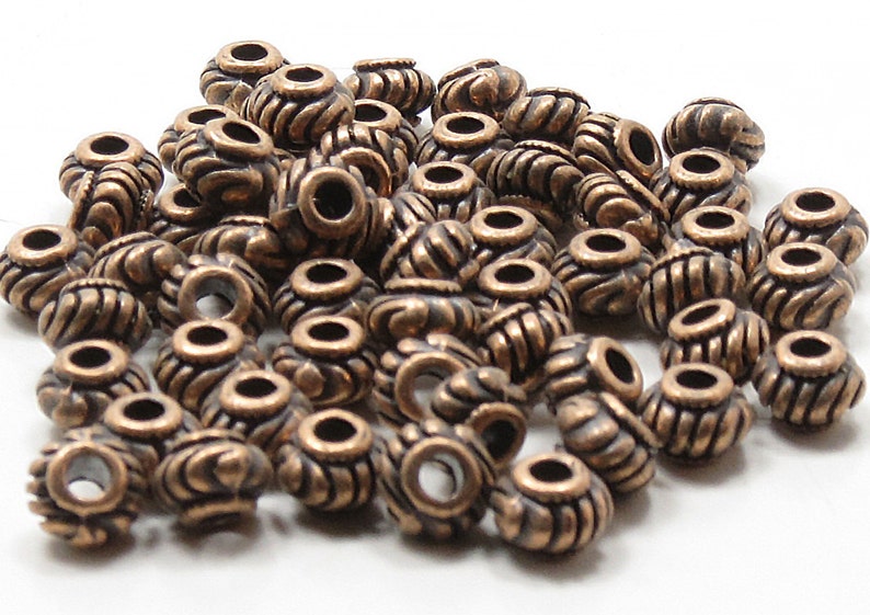 May include: A pile of antique copper-colored beads with a decorative design. The beads have a hole in the center for stringing.