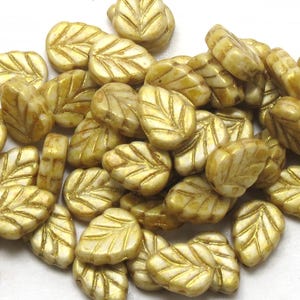 May include: A collection of gold leaf-shaped glass beads with a white iridescent finish. The beads have a raised leaf design and are perfect for jewelry making or crafting.