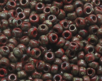 May include: A close-up of a pile of red and brown ceramic beads with white speckles. The beads are round and have a hole in the center.
