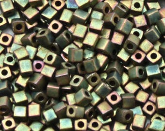 May include: A close-up of a pile of small, square, iridescent green beads. The beads have a metallic sheen and are perfect for jewelry making.