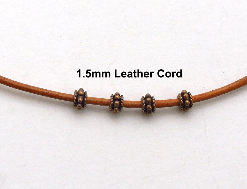 Puede incluir: Primer plano de un cord&oacute;n de cuero marr&oacute;n claro con cuatro cuentas de bronce antiguo. El texto "1.5mm Leather Cord" est&aacute; impreso en negro. Las cuentas tienen un dise&ntilde;o detallado y texturizado.