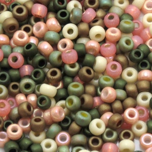 Könnte beinhalten: Eine Sammlung kleiner, runder Rocailles in verschiedenen Grüntönen, Braun-, Rosa- und Cremetönen. Die Perlen haben eine leicht irisierende Oberfläche.