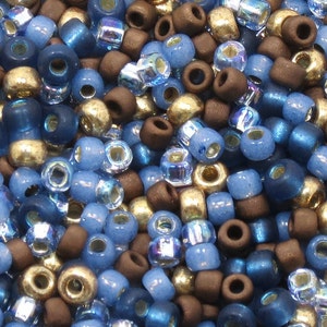 Könnte beinhalten: Ein Nahaufnahmebild einer Vielzahl kleiner, runder Perlen in Blautönen, Braun und Gold. Die Perlen sind in einem zufälligen Muster angeordnet, wodurch eine optisch ansprechende Textur entsteht.