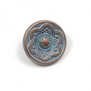 May include: A round, copper-colored button with a blue-green patina. The button features a detailed, embossed design of a six-pointed star with a smaller circle in the center.