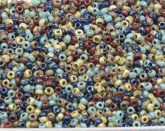 May include: A large assortment of small, round seed beads in various colors, including beige, blue, red, and brown. The beads have a speckled, textured finish.