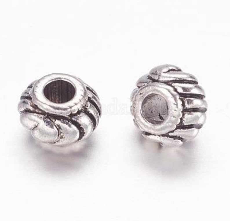 Op de afbeelding: Twee zilveren metalen kralencaps met een decoratief, getextureerd ontwerp. De kralencaps zijn rond van vorm met een gat in het midden.