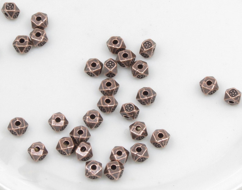 K&ouml;nnte beinhalten: Eine Gruppe kupferfarbener Metallperlen mit geometrischem Muster. Die Perlen haben ein Loch in der Mitte zum Auf f&auml;deln.