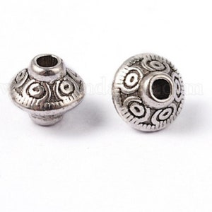May include: Two silver metal beads with a decorative, circular design. The beads have a hole in the center for stringing.