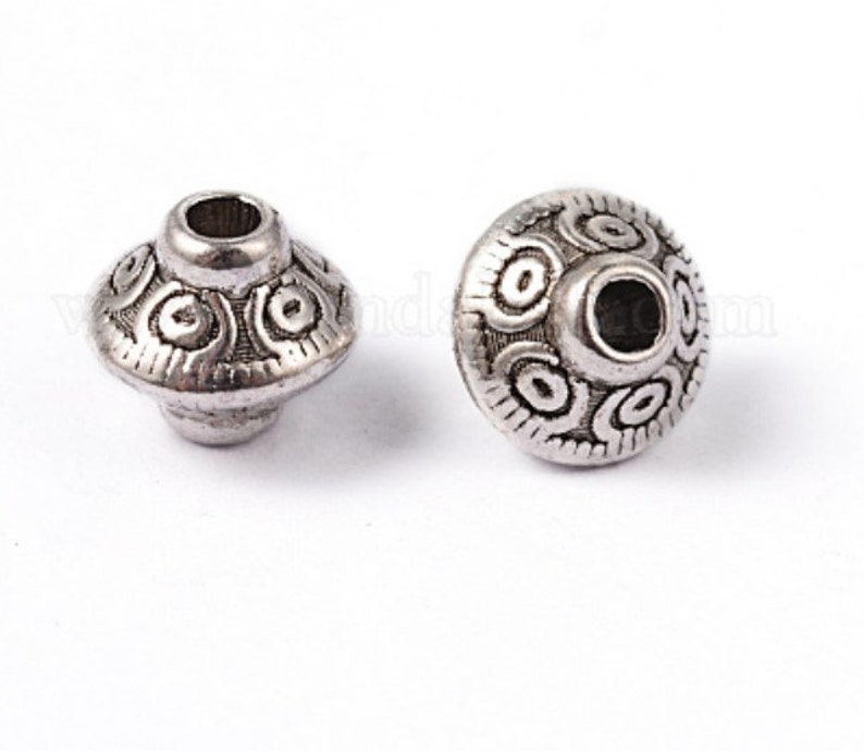 May include: Two silver metal beads with a decorative, circular design. The beads have a hole in the center for stringing.