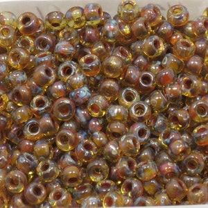 May include: A collection of small, round beads in shades of amber, brown, and hints of blue and purple. These beads have a hole through the center, perfect for stringing. Ideal for jewelry making and crafting projects.