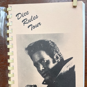 Könnte beinhalten: Ein Vintage-Heft mit einem Schwarzweißfoto eines Mannes in einer Lederjacke. Das Heft trägt den Titel "Dice Rules Tour" und das Jahr 1989 ist unten gedruckt.
