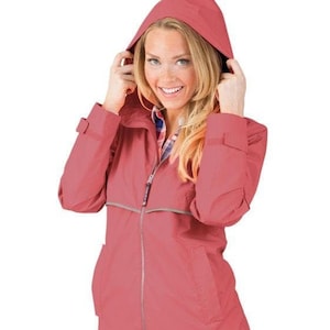May include: A coral pink rain jacket with a hood and a zipper closure. The jacket has a reflective trim around the zipper and pockets.