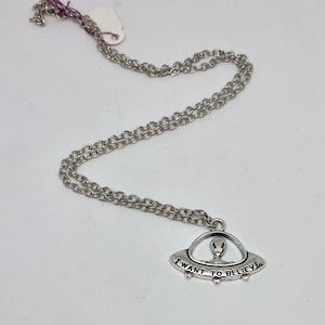 Op de afbeelding: Een zilveren ketting met een hanger in de vorm van een UFO. De hanger heeft de tekst "I want to believe" erop.