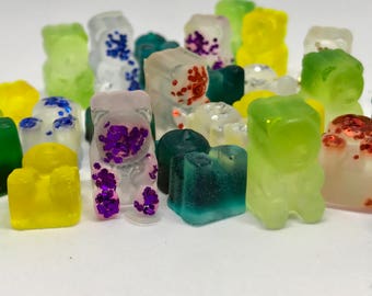 Könnte beinhalten: Eine Sammlung bunter Gummibärchen in Form von Bären. Die Gummibärchen bestehen aus klarem Gelee und haben verschiedene Farben, darunter Grün, Gelb, Rot, Lila und Weiß. Einige der Gummibärchen sind mit Glitzer oder Streuseln verziert.