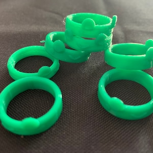 Puede incluir: Seis anillos de plástico verde con un diseño en relieve en el exterior. Los anillos están apilados uno encima del otro.