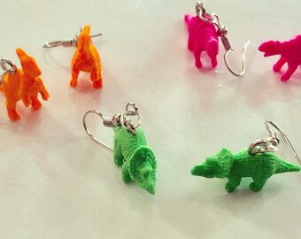Könnte beinhalten: Vier Paare Dinosaurier-Ohrringe. Zwei Paare sind grün, ein Paar ist pink und ein Paar ist orange. Die Ohrringe sind aus Kunststoff und haben silberne Haken.