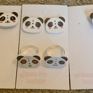 May include: Three white cards with panda bear designs. The top card has a single panda bear with black eyes and a pink nose. The middle card has two panda bears with black eyes and pink noses. The bottom card has two panda bears with black eyes and gray noses. The cards have the text "Dream Pop Boutique" printed on them.